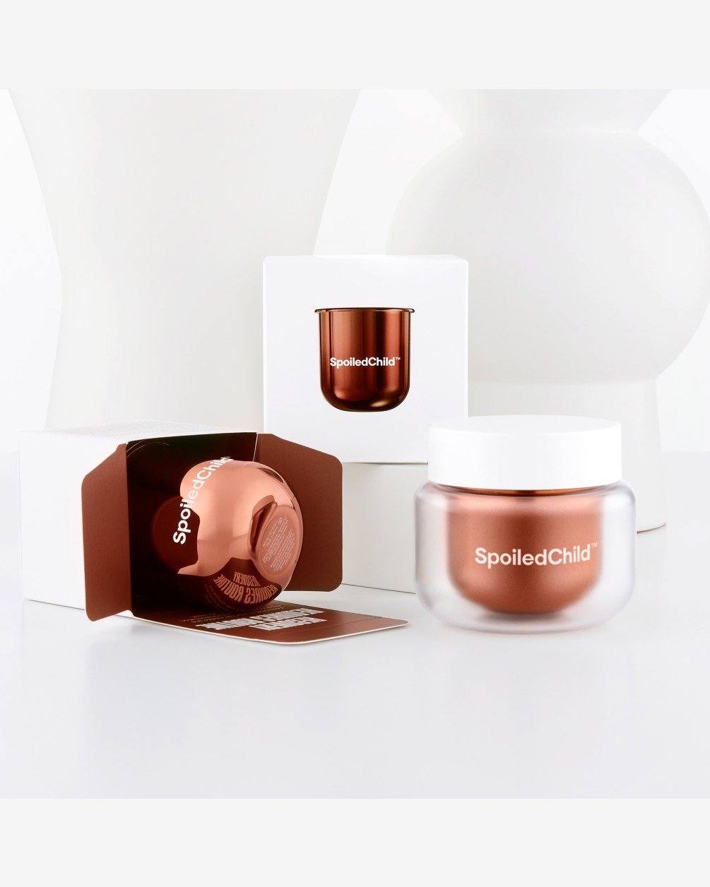 An overhead view of a disassembled SpoiledChild M26 Damage Reverser Hair Mask. A metallic copper refill capsule is floating between a white outer base and a white screw-top lid, demonstrating the refillable packaging design against a white background.