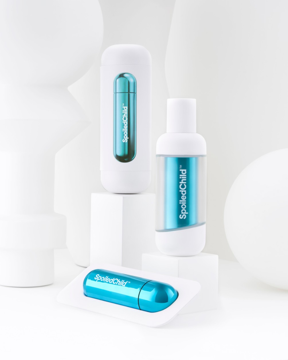 A product display featuring SpoiledChild S33 skincare items. It includes a tall white bottle, a white container with a teal capsule visible through a window, and a single teal refill capsule resting in the foreground on a white surface.